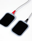 Pair of rectangular body treatment electrode pads with red and black connector cables for professional aesthetic machine treatments.